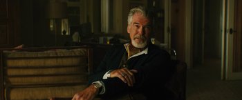 Movie still from “Black Adam” (2022), directed by Jaume Collet-Serra – An older man sitting in a chair wearing a suit and tie; Close Up shot, Over the shoulder angle