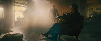 Movie still from “Black Adam” (2022), directed by Jaume Collet-Serra – A man sitting on a chair in a room with smoke coming out of the ceiling; Wide shot, Low angle