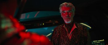 Movie still from “Black Adam” (2022), directed by Jaume Collet-Serra – An older man with a white beard is standing in front of a car; Medium shot, Over the shoulder angle