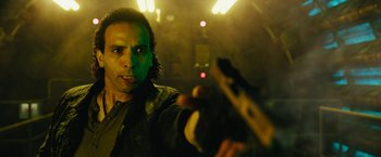 Movie still from “Black Adam” (2022), directed by Jaume Collet-Serra – A man is holding a gun in a dark room; Close Up shot, Low angle