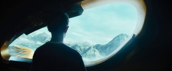 Movie still from “Black Adam” (2022), directed by Jaume Collet-Serra – A man looking out of a plane window at the mountains; Medium shot, Over the shoulder angle