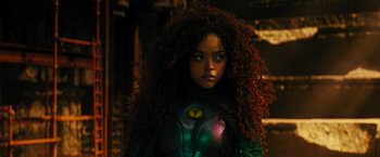Movie still from “Black Adam” (2022), directed by Jaume Collet-Serra – A woman with long curly red hair wearing a green and black costume; Close Up shot, Over the shoulder angle