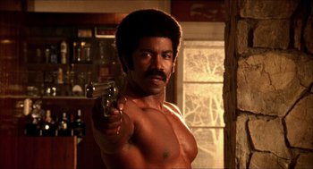 A shirtless man with a gun pointing at the camera