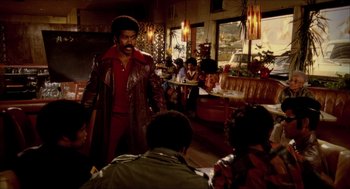 A man wearing a brown leather jacket in front of a group of people in a restaurant