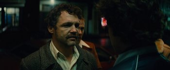Movie still from “Black Mass” (2015), directed by Scott Cooper – A man with a beard is talking to two other men; Close Up shot, Over the shoulder angle