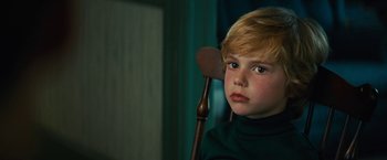 A boy with blonde hair sitting in a wooden chair