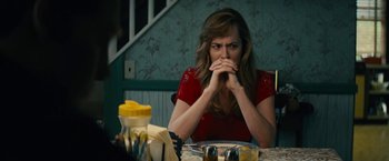 Movie still from “Black Mass” (2015), directed by Scott Cooper – A woman sitting at a table with her hands over her mouth; Medium shot, Over the shoulder angle