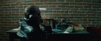 Movie still from “Black Mass” (2015), directed by Scott Cooper – A man sitting at a table talking on a phone; Medium shot, Over the shoulder angle
