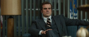 Movie still from “Black Mass” (2015), directed by Scott Cooper – A man in a suit and tie sitting in front of a window; Close Up shot, Low angle