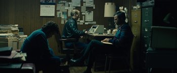 Movie still from “Black Mass” (2015), directed by Scott Cooper – Two men sitting at a table in front of a laptop computer; Wide shot, High angle