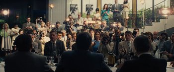 Movie still from “Black Mass” (2015), directed by Scott Cooper – A group of people sitting around a table with microphones; Wide shot, Over the shoulder angle