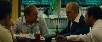 Movie still from “Black Mass” (2015), directed by Scott Cooper – Two men are sitting at a table with drinks; Medium shot, Over the shoulder angle