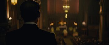 Movie still from “Black Mass” (2015), directed by Scott Cooper – A man in a black suit sitting in front of an altar; Medium shot, Low angle