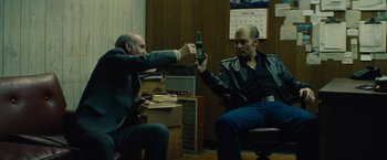 Movie still from “Black Mass” (2015), directed by Scott Cooper – Two men sitting in a room one is holding a beer; Medium shot, Low angle