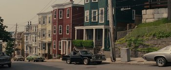 Movie still from “Black Mass” (2015), directed by Scott Cooper – A car parked on the side of the road in front of a row of houses; Extreme Wide shot, High angle
