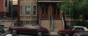 Movie still from “Black Mass” (2015), directed by Scott Cooper – A car parked on the side of the road next to a building; Wide shot, High angle