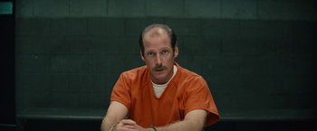 Movie still from “Black Mass” (2015), directed by Scott Cooper – A man in an orange prison uniform sitting in front of a green wall; Close Up shot, Over the shoulder angle