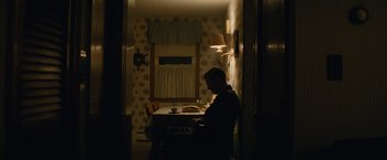 Movie still from “Black Mass” (2015), directed by Scott Cooper – A man sitting at a table in a dark room; Wide shot, High angle