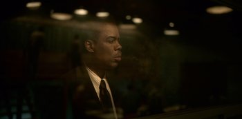 Movie still from “Fargo” (2014), created by Noah Hawley – A man wearing a suit and tie smoking a cigarette in front of a window; Close Up shot, Over the shoulder angle