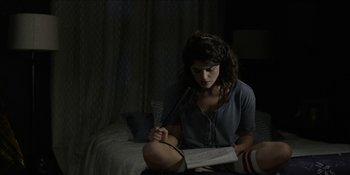 Movie still from “Blair Witch” (2016), directed by Adam Wingard – A woman sitting on the ground reading a newspaper; Medium shot, High angle