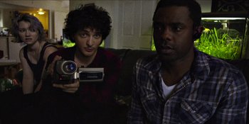 Movie still from “Blair Witch” (2016), directed by Adam Wingard – A man and a woman sitting on a couch holding a video camera; Medium shot, High angle