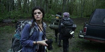 Movie still from “Blair Witch” (2016), directed by Adam Wingard – A woman holding a camera while standing in the woods; Medium shot, Low angle