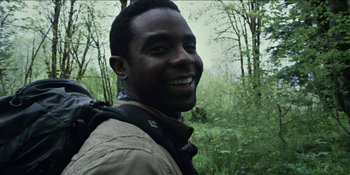 Movie still from “Blair Witch” (2016), directed by Adam Wingard – A man smiling for the camera in a wooded area; Close Up shot, Low angle