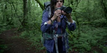 Movie still from “Blair Witch” (2016), directed by Adam Wingard – A woman with a backpack holding a camera in the woods; Medium shot, Low angle