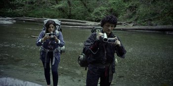 Movie still from “Blair Witch” (2016), directed by Adam Wingard – A man and a woman taking pictures in the water; Medium shot, Low angle