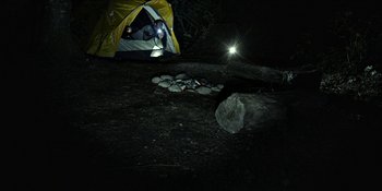 Movie still from “Blair Witch” (2016), directed by Adam Wingard – A person is camping in the dark with a flashlight; Wide shot, High angle