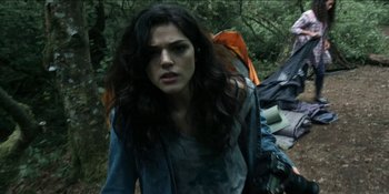 Movie still from “Blair Witch” (2016), directed by Adam Wingard – A woman with long dark hair is walking through the woods; Medium shot, Low angle