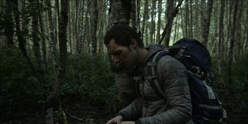 Movie still from “Blair Witch” (2016), directed by Adam Wingard – A man with a backpack in the woods looking down; Close Up shot, Low angle