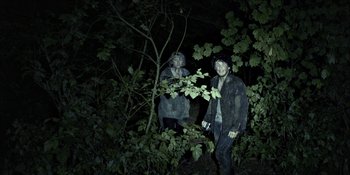 Movie still from “Blair Witch” (2016), directed by Adam Wingard – A couple of people standing next to some bushes; Wide shot, High angle