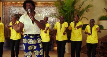 Movie still from “Blended” (2014), directed by Frank Coraci – A group of men in yellow shirts singing into microphones; Medium shot, Low angle