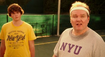 Movie still from “Blended” (2014), directed by Frank Coraci – Two men standing on a tennis court with tennis balls in the background; Medium shot, Over the shoulder angle