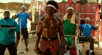 Movie still from “Blended” (2014), directed by Frank Coraci – A group of men working out together in a gym; Medium shot, Over the shoulder angle