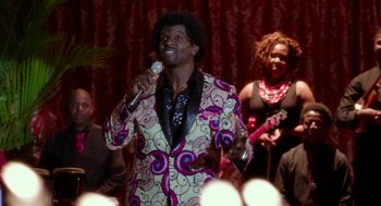 Movie still from “Blended” (2014), directed by Frank Coraci – A man in a colorful suit singing into a microphone; Medium shot, Over the shoulder angle