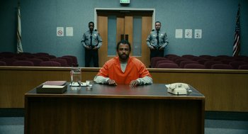 Movie still from “Blindspotting” (2018), directed by Carlos López Estrada – A man sitting at a table in an orange jail cell; Wide shot, Low angle