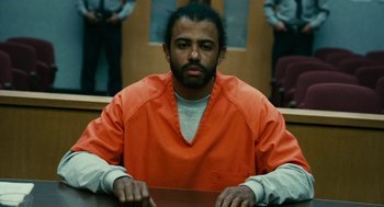 Movie still from “Blindspotting” (2018), directed by Carlos López Estrada – A man in an orange prison uniform sitting at a table in a courtroom; Medium shot, Low angle