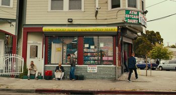 Movie still from “Blindspotting” (2018), directed by Carlos López Estrada – Two people sitting on the side of the street outside of a store; Wide shot, Low angle