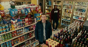Movie still from “Blindspotting” (2018), directed by Carlos López Estrada – A man standing in front of a store filled with lots of food; Wide shot, High angle