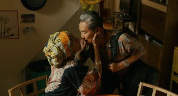 Movie still from “Blindspotting” (2018), directed by Carlos López Estrada – An older man and a younger woman are touching their noses together; Medium shot, High angle