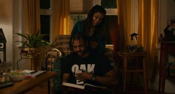 Movie still from “Blindspotting” (2018), directed by Carlos López Estrada – A man and a woman are reading a book together; Medium shot, Over the shoulder angle