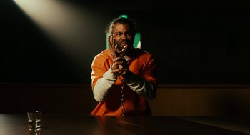 Movie still from “Blindspotting” (2018), directed by Carlos López Estrada – A man in an orange shirt is holding a chain; Medium shot, High angle