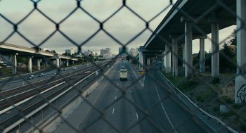 Movie still from “Blindspotting” (2018), directed by Carlos López Estrada – A van driving down a street through a chain link fence; Extreme Wide shot, High angle