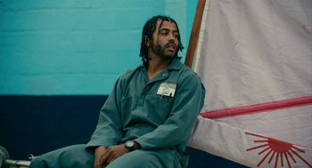 Movie still from “Blindspotting” (2018), directed by Carlos López Estrada – A man sitting on a chair in a room; Medium shot, Low angle