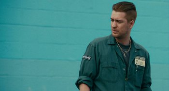 Movie still from “Blindspotting” (2018), directed by Carlos López Estrada – A man standing in front of a blue brick wall; Medium shot, Over the shoulder angle