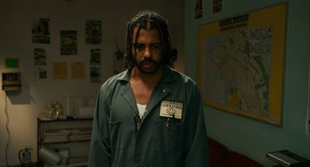 Movie still from “Blindspotting” (2018), directed by Carlos López Estrada – A man with dreadlocks standing in front of a map; Medium shot, Low angle
