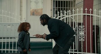 Movie still from “Blindspotting” (2018), directed by Carlos López Estrada – A man and a little girl standing in front of a building; Medium shot, Low angle