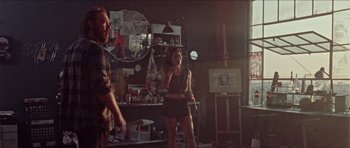 Movie still from “Bliss” (2019), directed by Joe Begos – A woman standing in front of a man in a room; Wide shot, Low angle